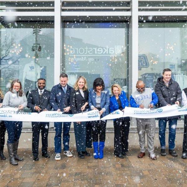 A group of people stand outside a modern building cutting a ribbon with scissors.