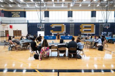 tables in a gymnasium with people seated around them; head table has blue drapes with GVSU logo. 背景中的露天看台是蓝色的，上面有大大的金色的B和C