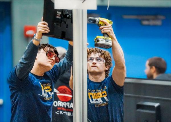 two team members from East Grand Rapids hold a drill and fix their robot