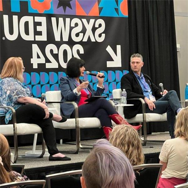 President Mantella sits on a stage between other panelists and speaks into a microphone.